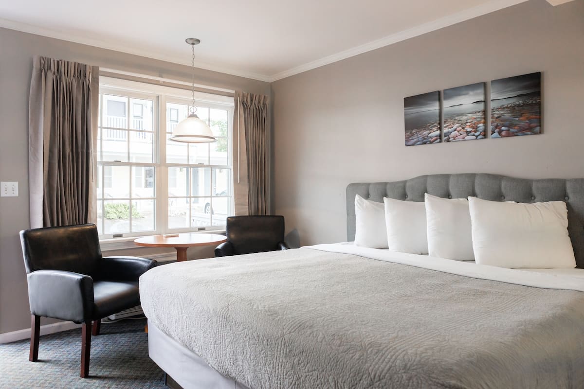 A hotel room with a large bed, two chairs, a small table, and a window with curtains.
