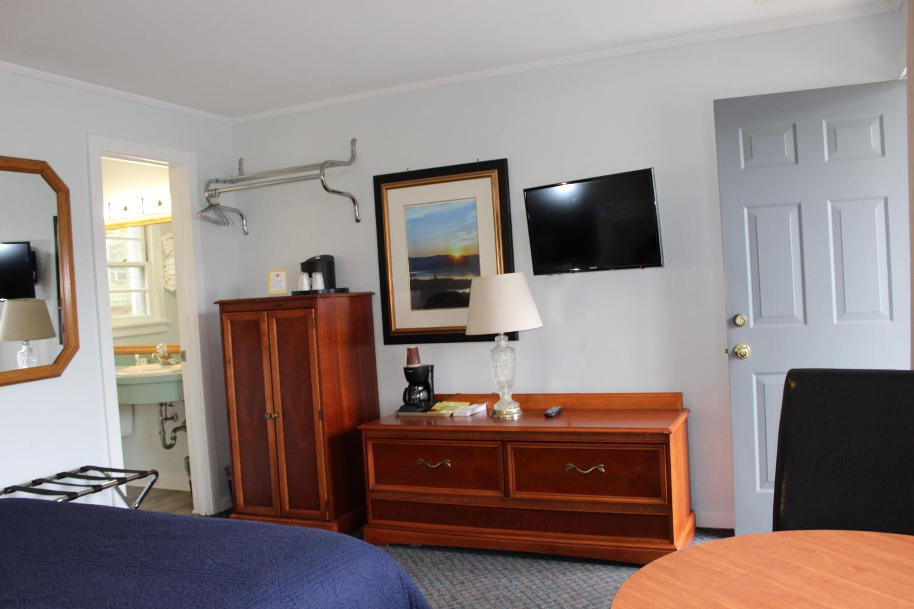 A hotel room with a bed, a wooden dresser, a desk, a chair, a television, and a door.