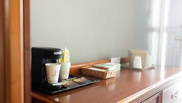 A coffee station with a coffee maker, cups, and a basket of pastries on a wooden counter.