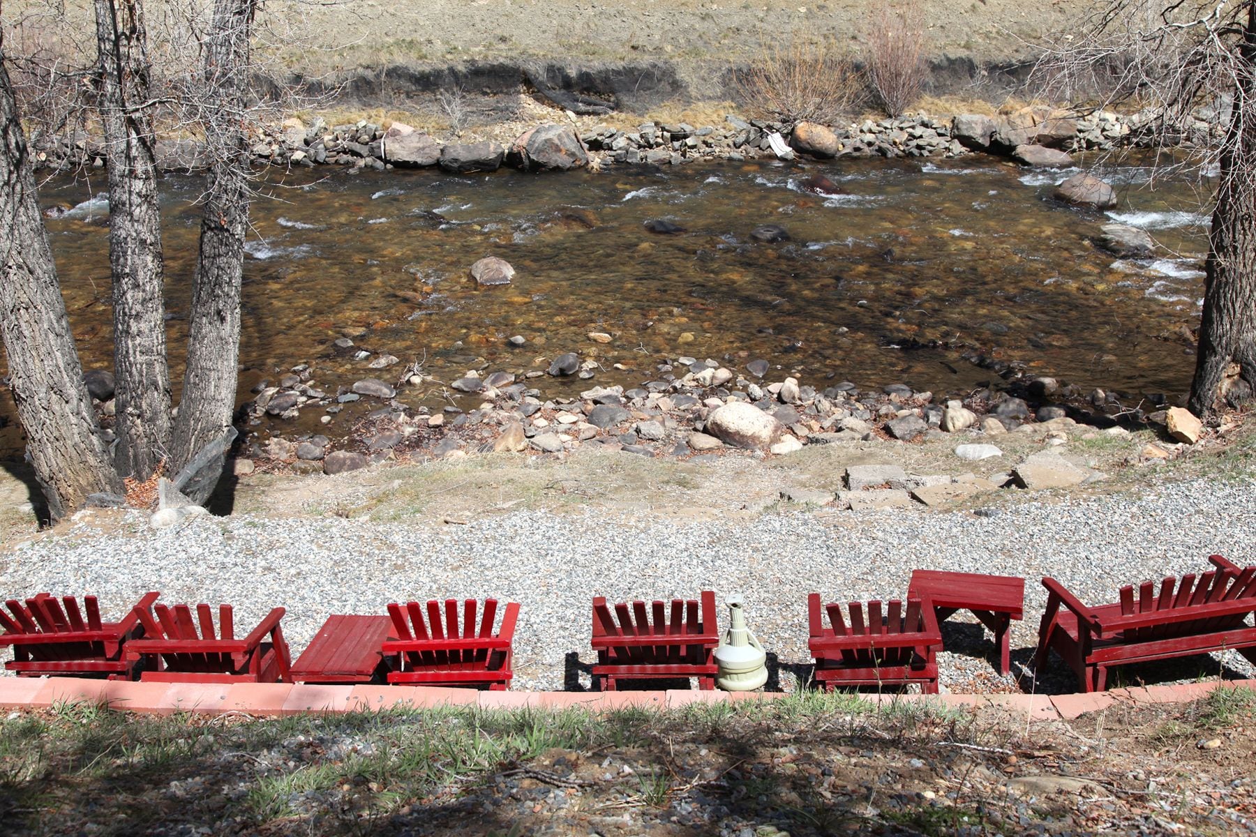 A riverside seating area with red Adirondack chairs and a stone wall.