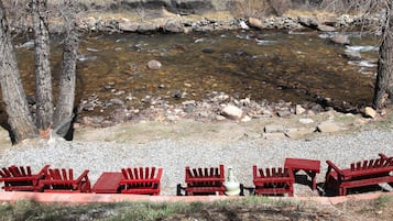 A riverside seating area with red Adirondack chairs and a stone wall.