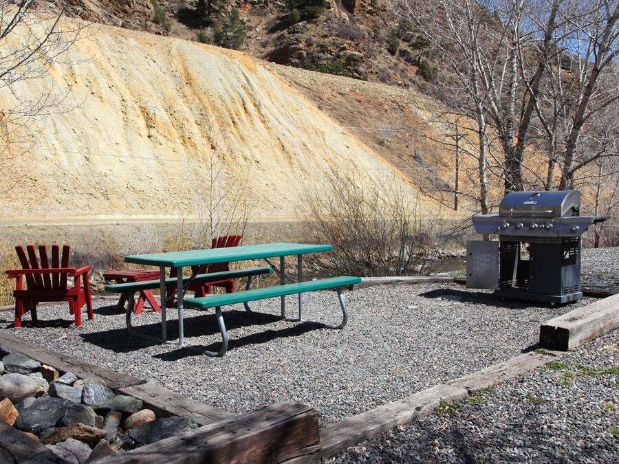 Un espace pique-nique avec des tables et des chaises de pique-nique rouges et vertes, un barbecue et une colline rocheuse en arrière-plan.
