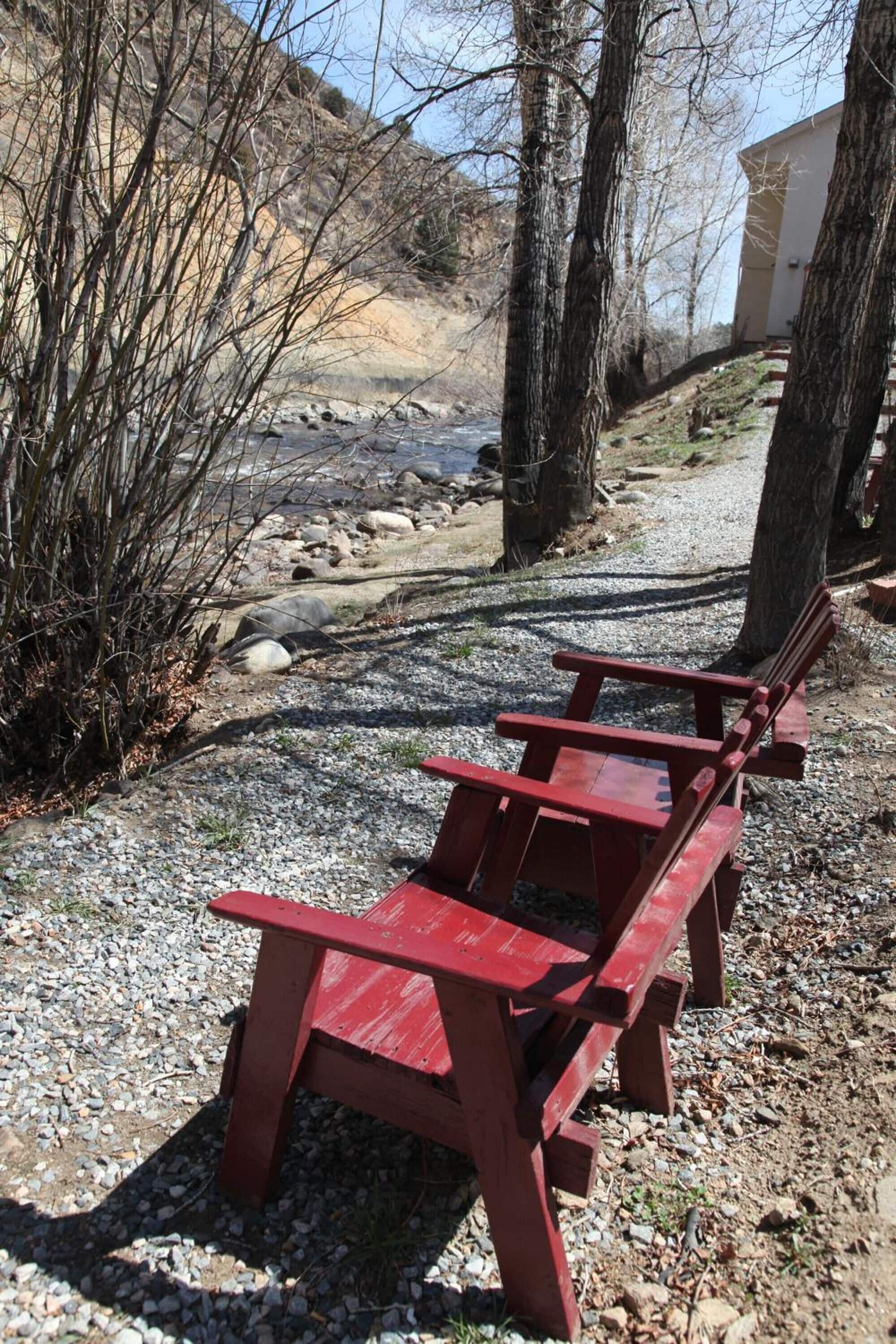 A red wooden bench in a gravel area with trees and a building in the background.