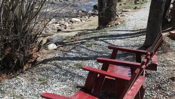 A red wooden bench in a gravel area with trees and a building in the background.