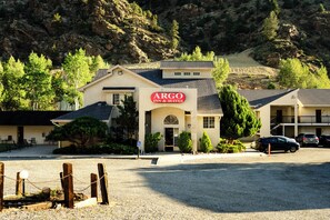 A building with a sign for ARGO INN & SUITES, a parking area, and a mountainous backdrop. - Argo Inn and Suites (Idaho Springs)