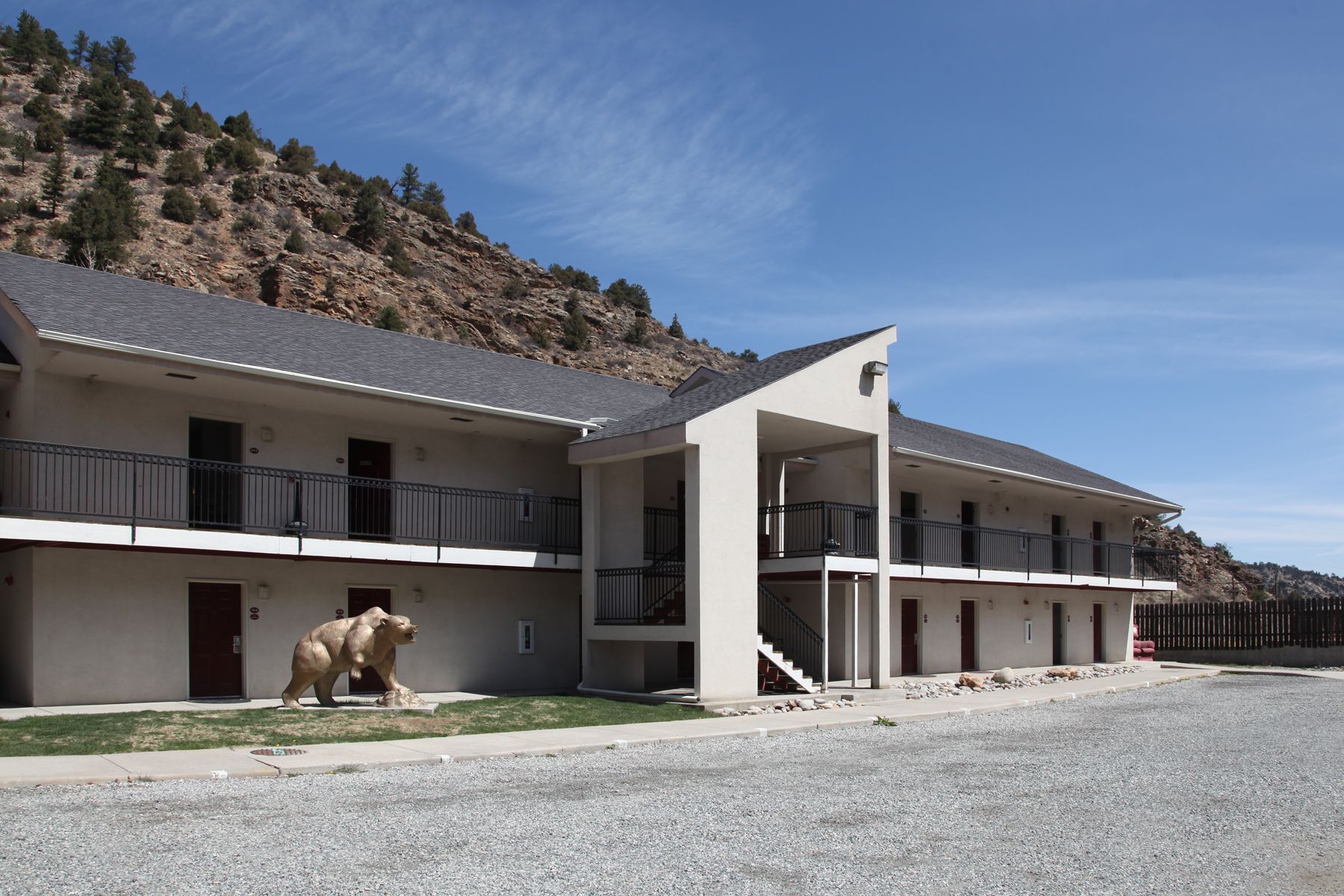 Un motel de dos pisos con entrada central, un área de estar al aire libre cubierta y una estatua de un oso.