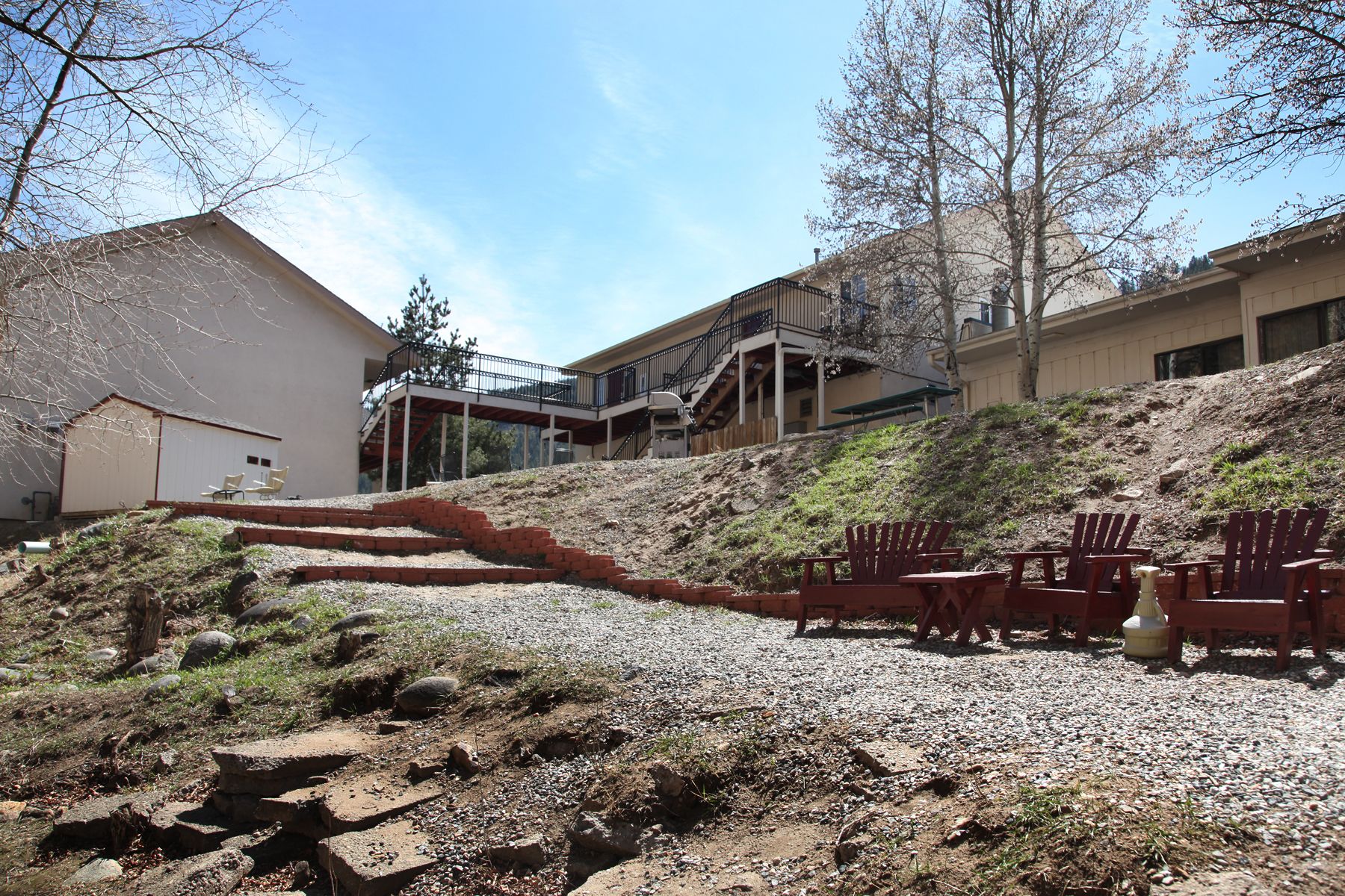 A building with a covered outdoor seating area, a staircase leading to a second floor, and a gravel path.