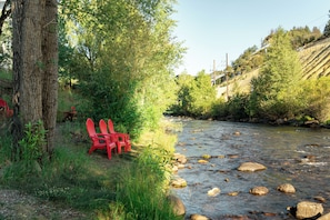 A river with rocks, a tree, and red chairs by the water. - Argo Inn and Suites (Idaho Springs)