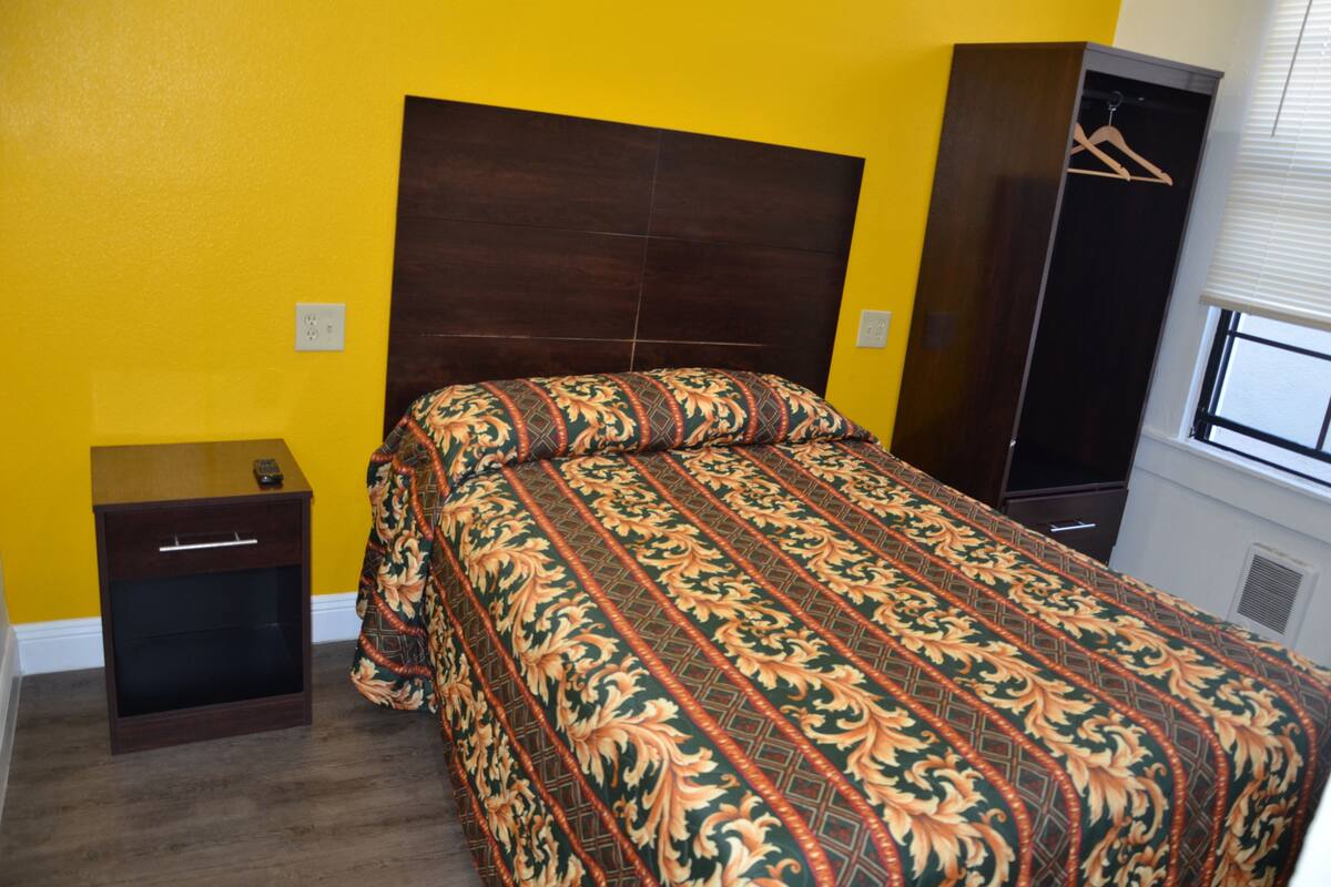 A bedroom with a bed, a nightstand, a wardrobe, and a window.