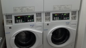 A row of stacked front-loading washing machines with digital displays and operating instructions. - Hotel Sunrise (San Francisco)