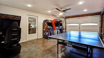Une pièce équipée d’une table de ping-pong, de jeux d’arcade et d’un ventilateur au plafond.