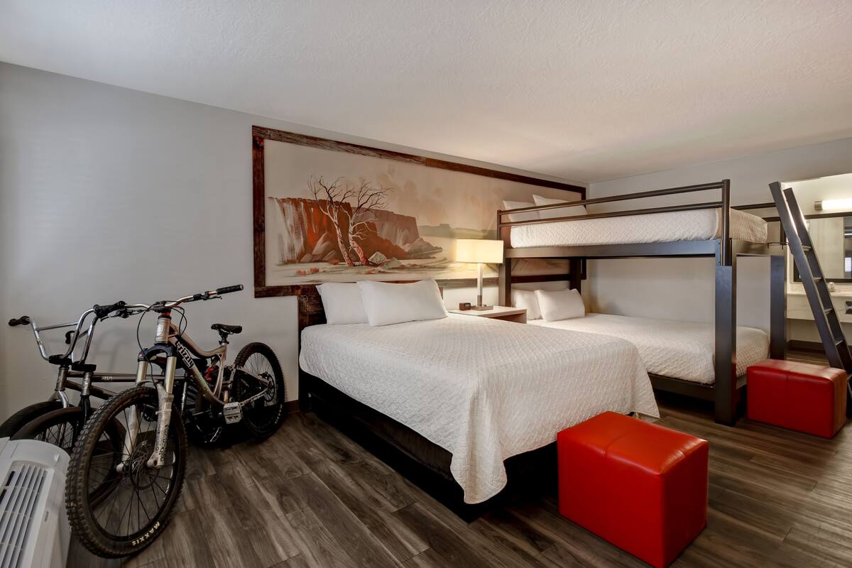 A hotel room with a bunk bed, a bicycle, and a painting on the wall.
