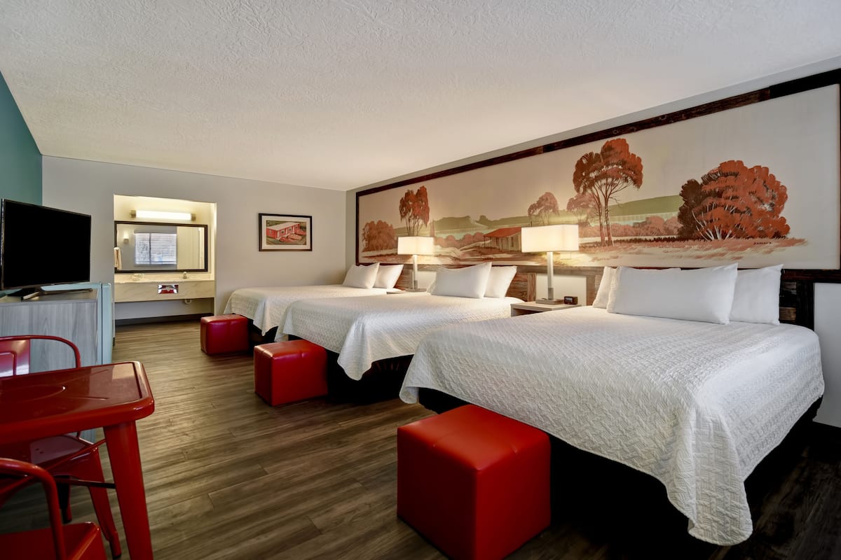 A hotel room with two beds, a TV, a desk, and a painting on the wall.
