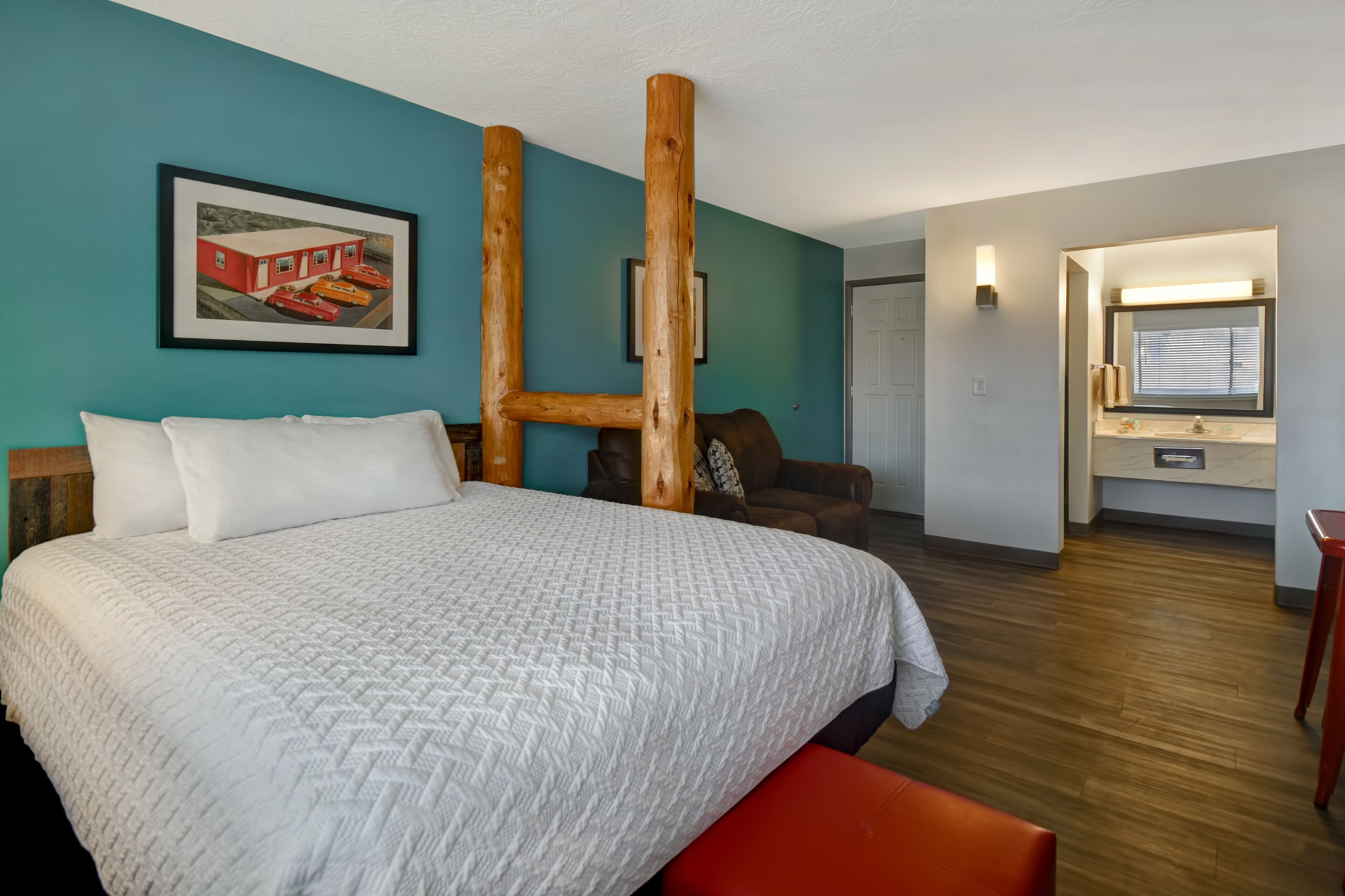A hotel room with a large bed, a wooden pillar structure, a framed picture on the wall, and a bathroom visible through an open door.