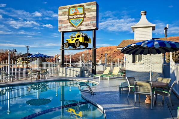 A pool area with lounge chairs, a sign for 'Expedition Lodge', and a desert landscape in the background. - Expedition Lodge Moab Arches National Park (Moab)