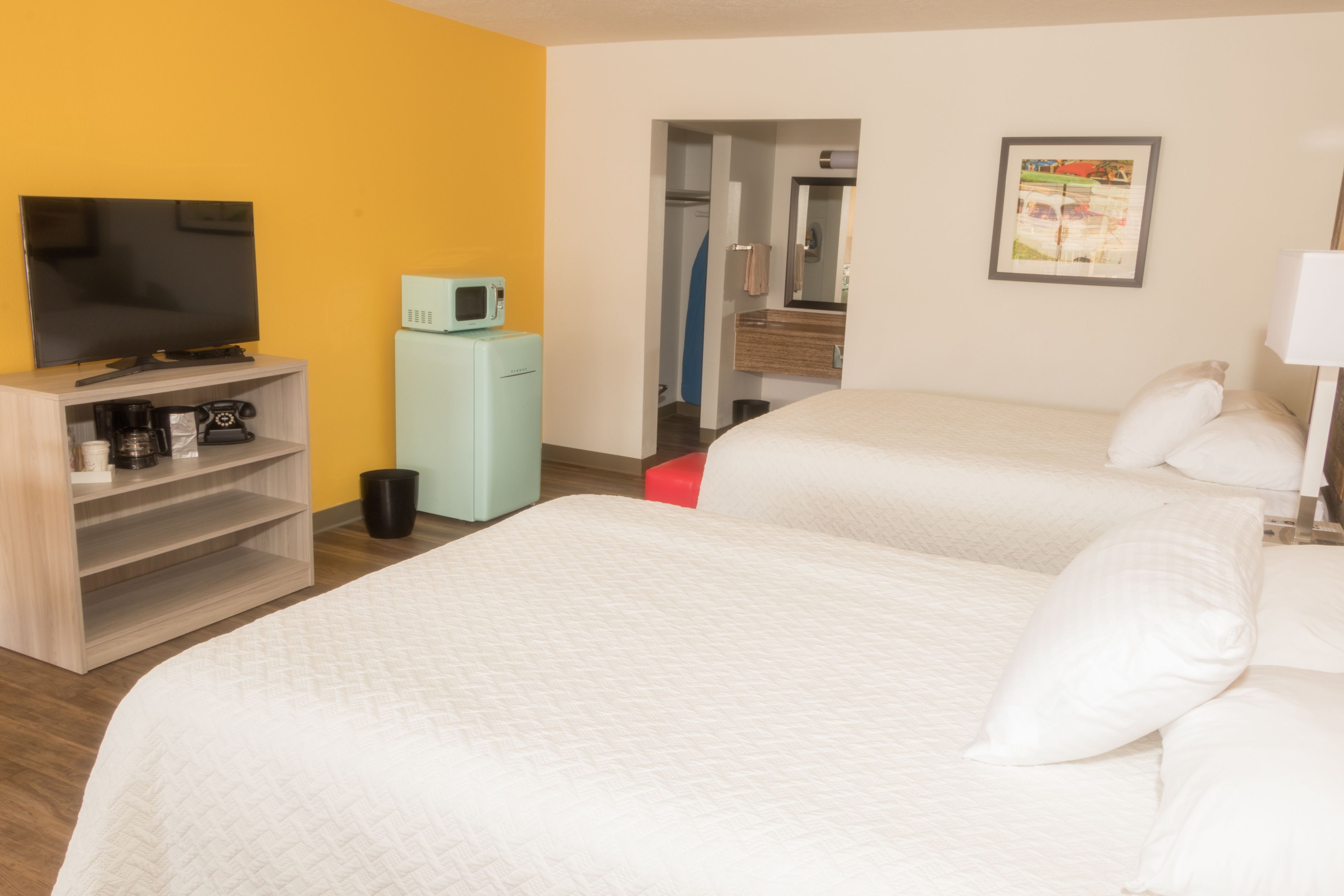A hotel room with two beds, a TV, a microwave, a coffee maker, and a mirror.