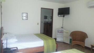 Quarto de hotel com duas camas, uma televisão fixada na parede, uma mesa de trabalho com uma cadeira e um guarda-roupa.