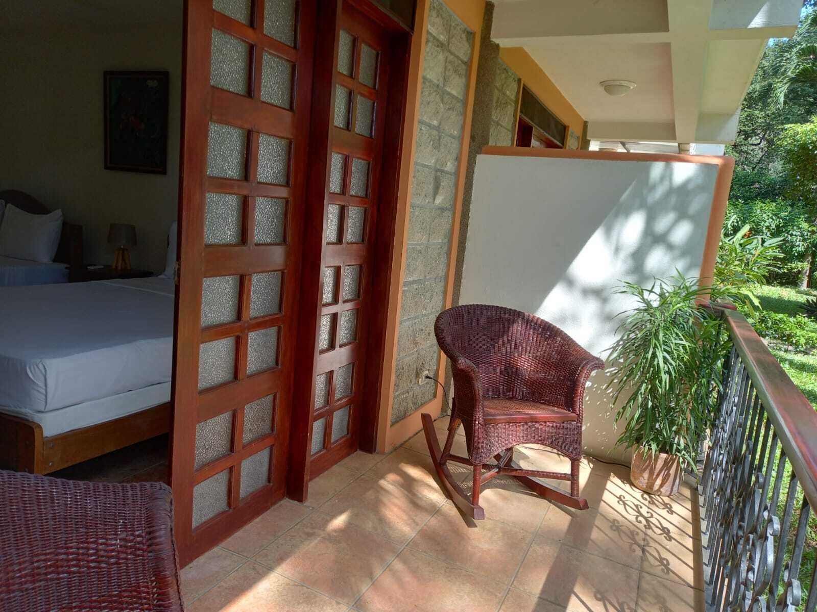A bedroom with a bed, a wooden door with glass panels, a wicker chair, and a potted plant.