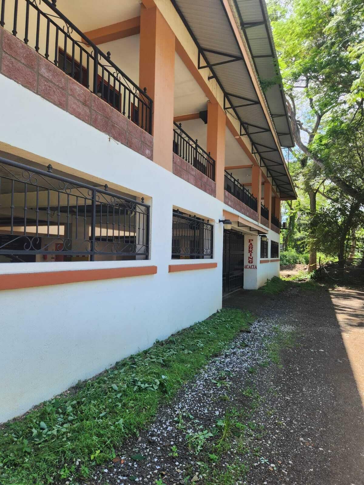 Un edificio con fachada blanca, varios balcones y un camino de grava que lleva a la entrada.