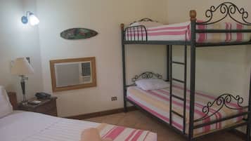 Una stanza con un letto a castello, un letto singolo, un comodino con una lampada, una sveglia a muro e un piatto decorativo.