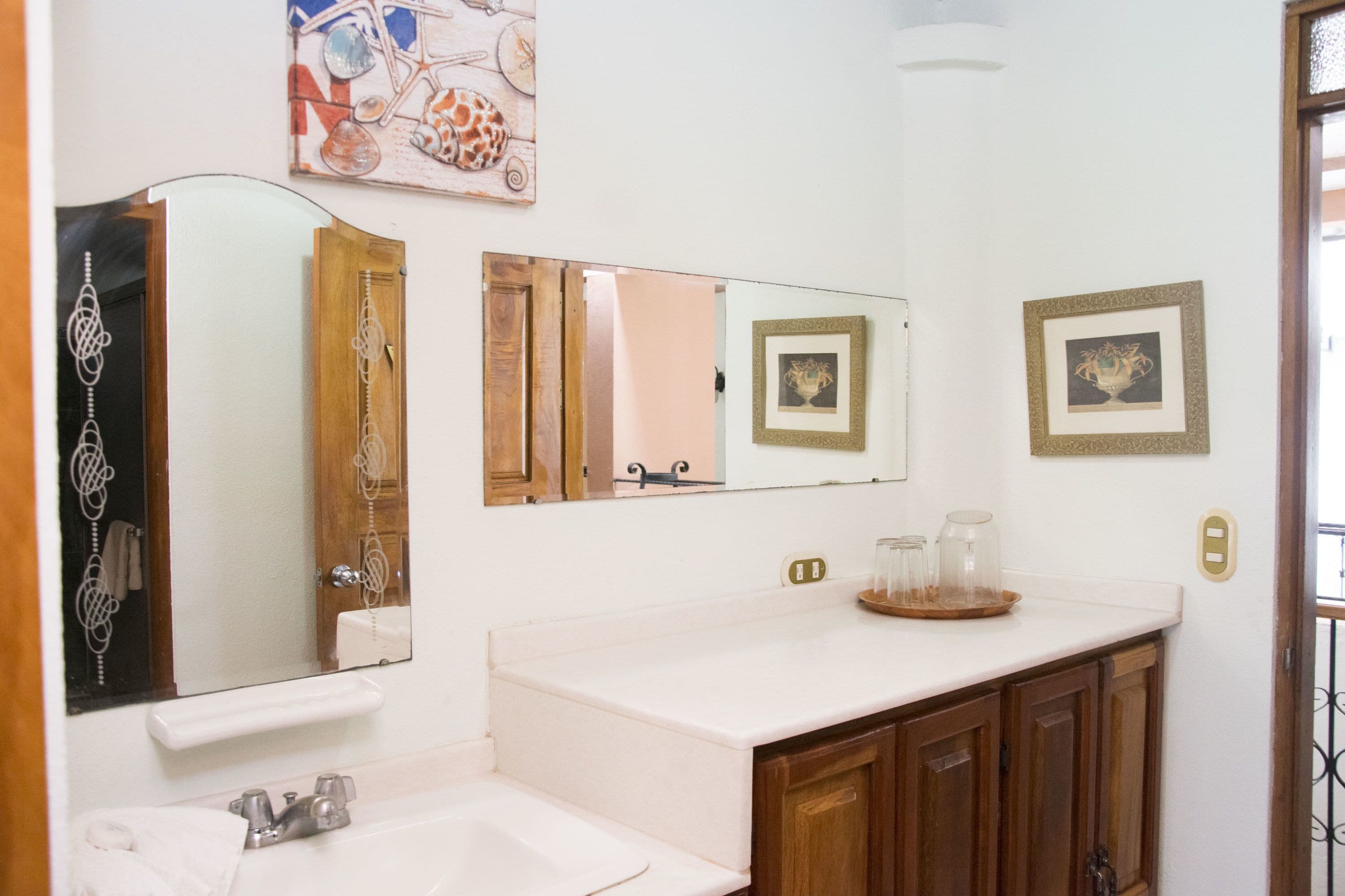 A bathroom with a white sink, wooden cabinets, a mirror, and decorative items on the wall.
