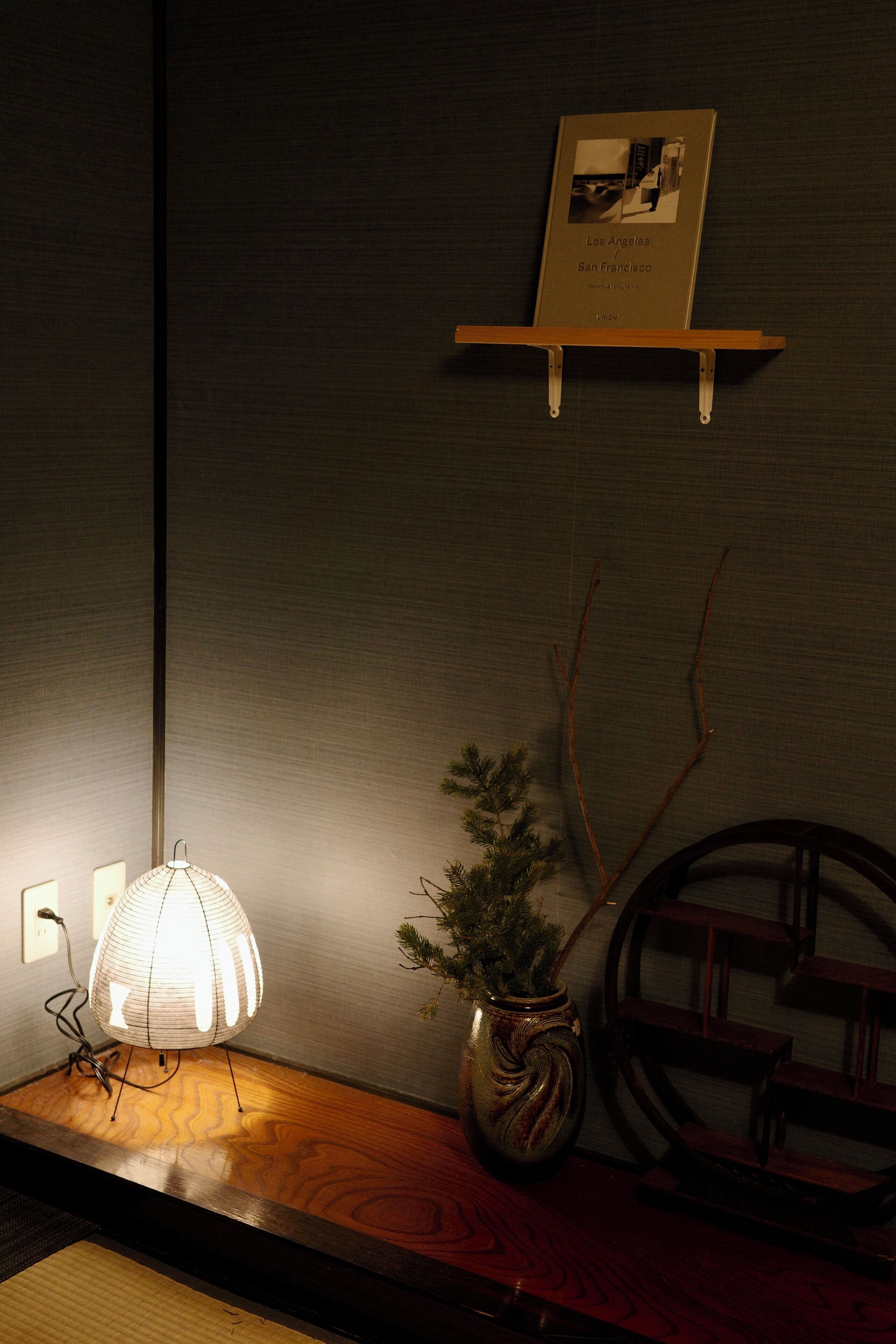 A room with a wooden table, a lamp, a framed picture, and a small potted plant.