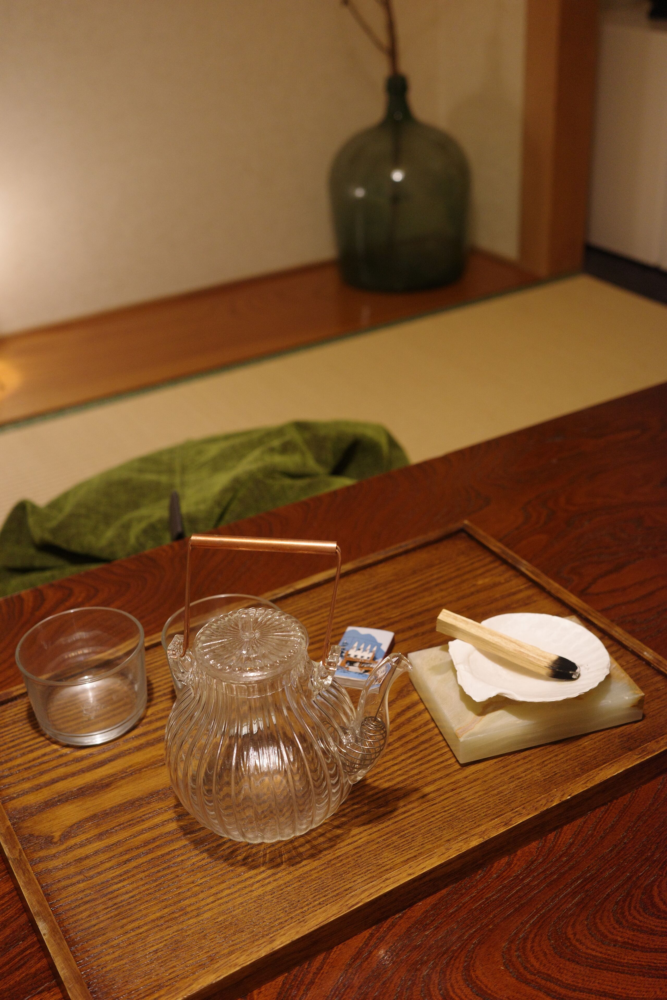 A wooden tray with a glass teapot, a cup, and a small wooden box on a table.