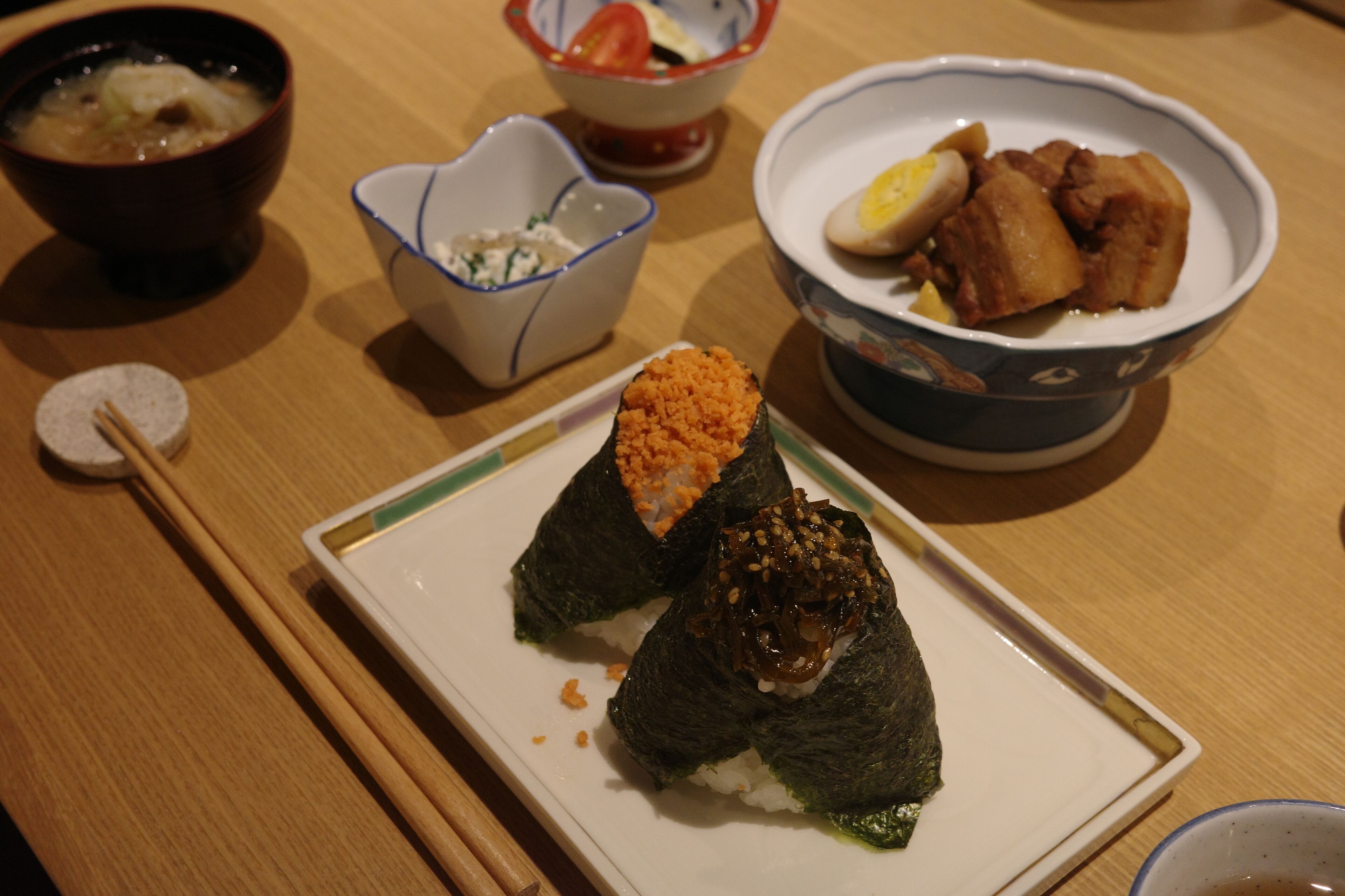 Une table à manger avec une assiette de sushis, un bol de soupe et un bol de plats frits.