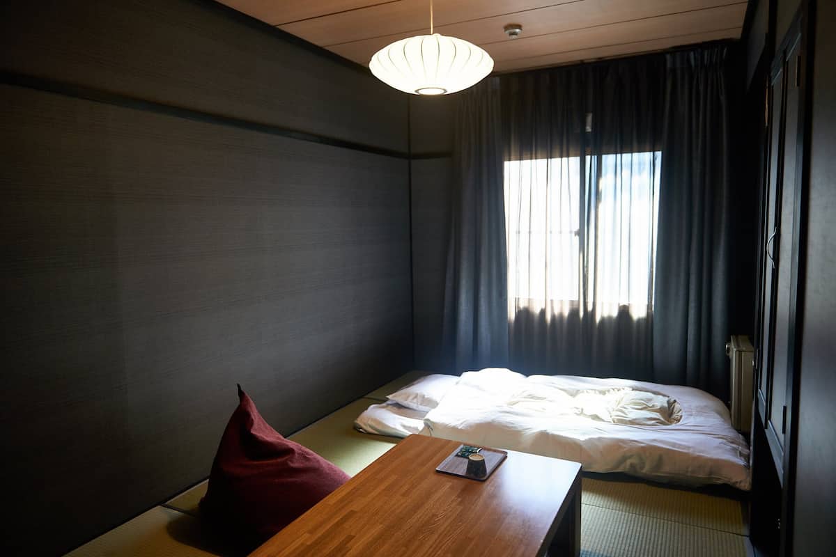 Une chambre d’hôtel avec un lit, une table en bois, un oreiller rouge et un luminaire au plafond.