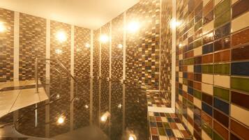 A modern bathroom with a tiled floor and walls, a glass shower enclosure, and a metal handrail.