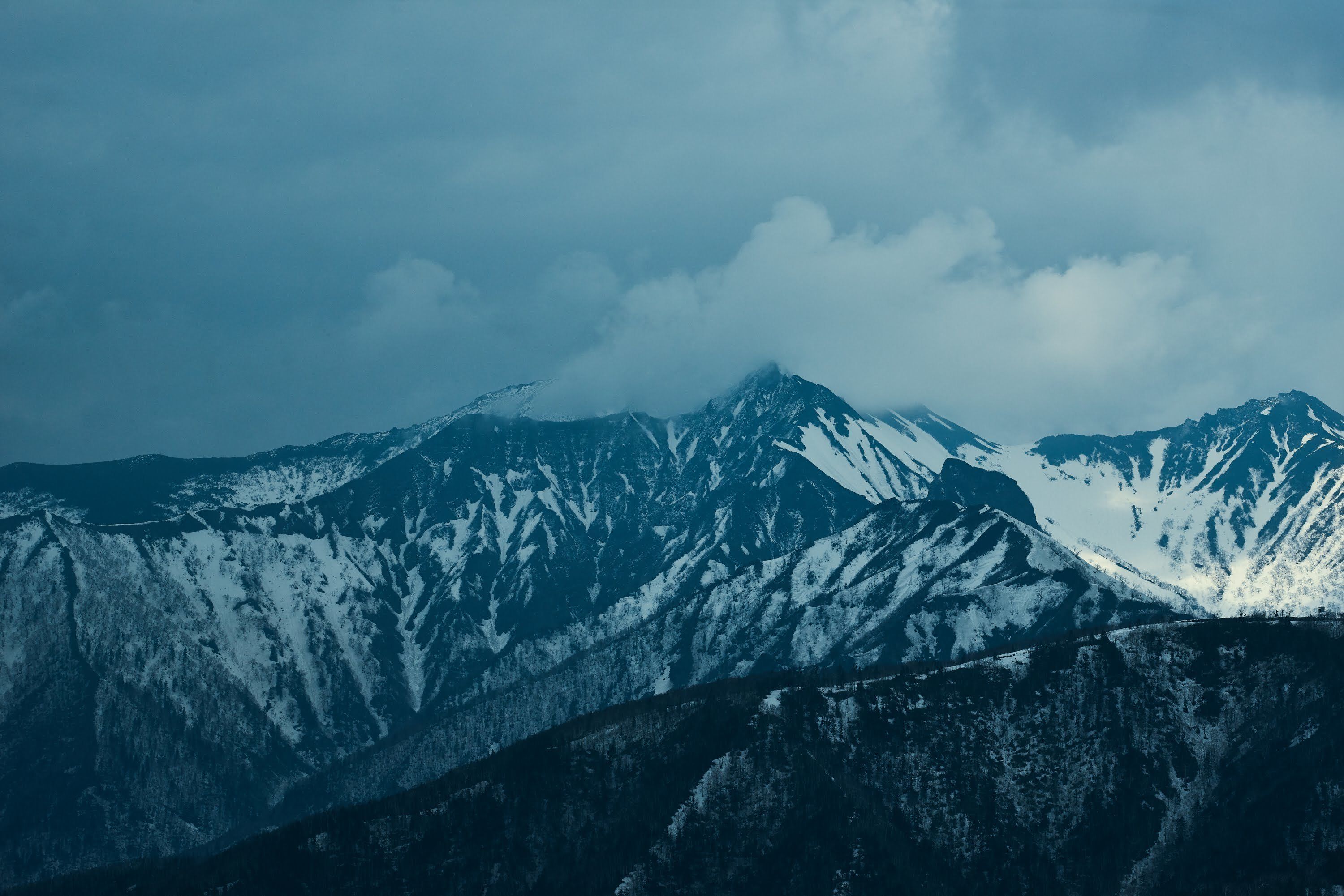 A mountain range with snow-covered peaks and a cloudy sky.