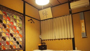 A hotel room with a quilted wall hanging, a bed with a floral bedspread, a hanging rack, and a wall-mounted air conditioner. - Kakure-Yado Yuji-inn - Hostel (Kurashiki)