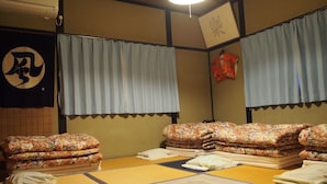 A tatami mat room with futons, a shoji screen, and a hanging shifu. - Kakure-Yado Yuji-inn - Hostel (Kurashiki)