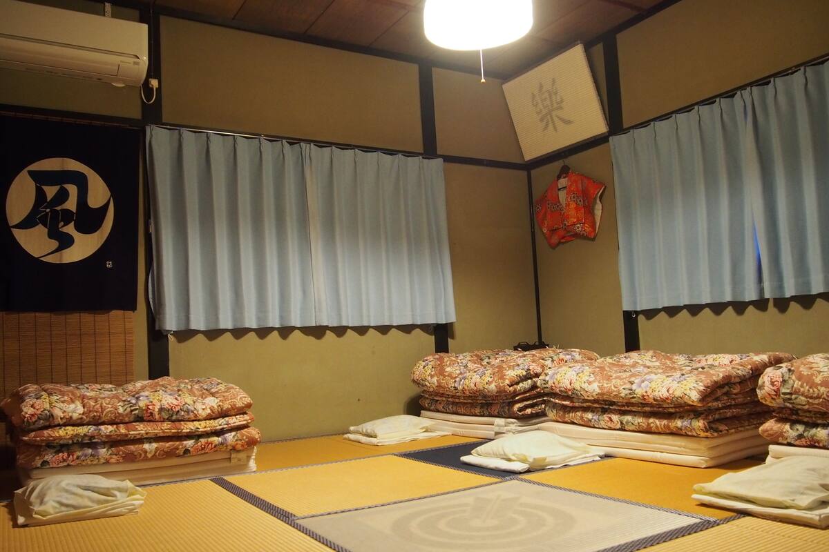 A tatami mat room with futons, a shoji screen, and a hanging shifu.