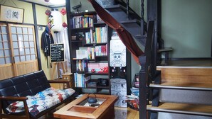 A cozy room with a sofa, a wooden coffee table, a bookshelf, and a staircase. - Kakure-Yado Yuji-inn - Hostel (Kurashiki)