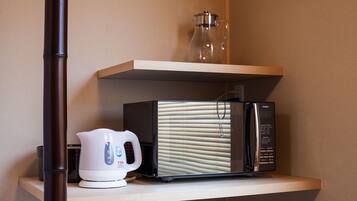A kitchen area with a microwave, a kettle, and a glass pitcher on a shelf.