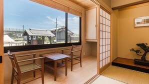 A traditional Japanese room with tatami flooring, a low table with two chairs, a shoji screen, and a bonsai tree. - Racine Home Harie (Takashima)