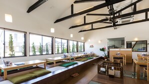 A modern restaurant with long wooden benches and tables, large windows, and a ceiling fan. - Racine Home Harie (Takashima)