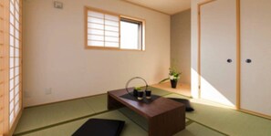 A traditional Japanese room with tatami flooring, a low wooden table with a tea set, a shoji screen window, and a door with a sliding mechanism.