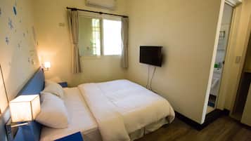 A hotel room with a bed, a TV, a window with curtains, a bedside lamp, and a wall-mounted air conditioner.