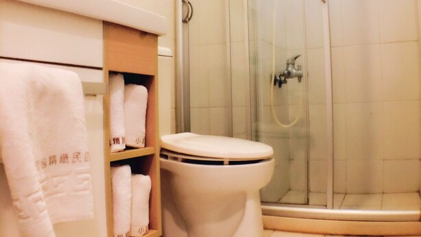A bathroom with a toilet, a glass shower enclosure, and a shelf with towels. - backpackers.INN (Jinning)