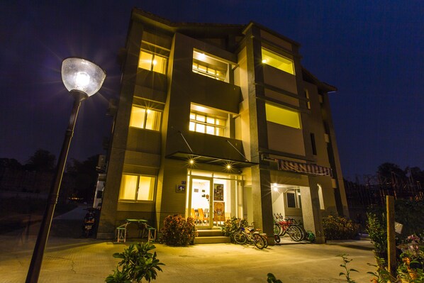 A multi-story building with a well-lit entrance, a bicycle parked outside, and a street lamp in the foreground. - backpackers.INN (Jinning)