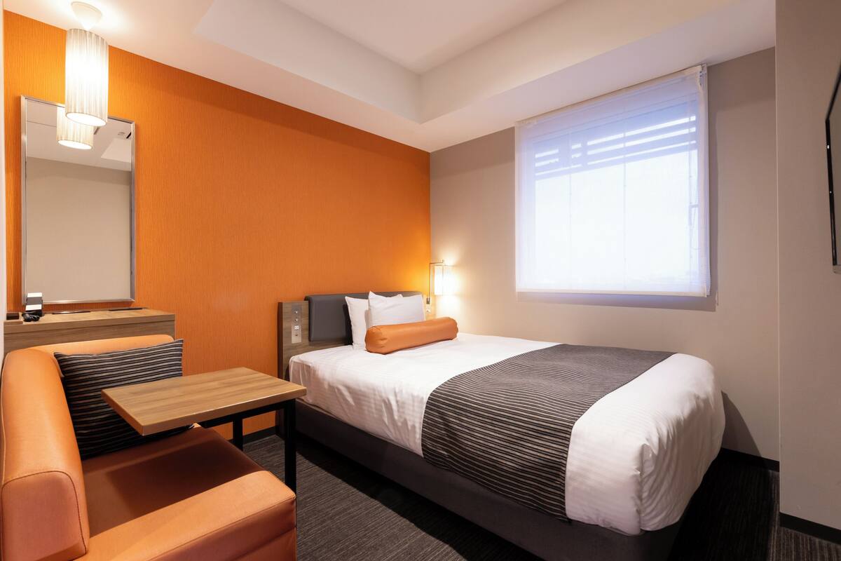 A modern hotel room with a bed, a sofa, a small table, and a mirror.