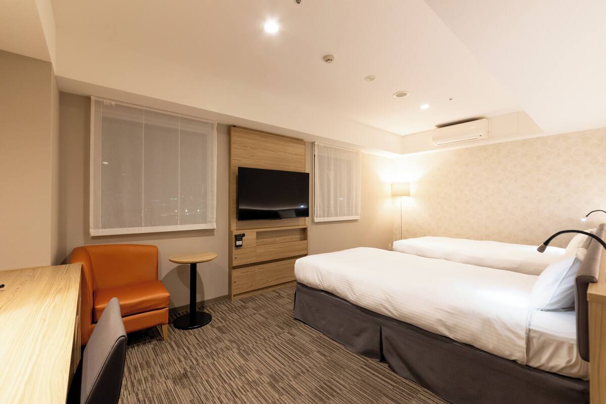 A hotel room with a bed, a TV, a chair, a desk, and a lamp.