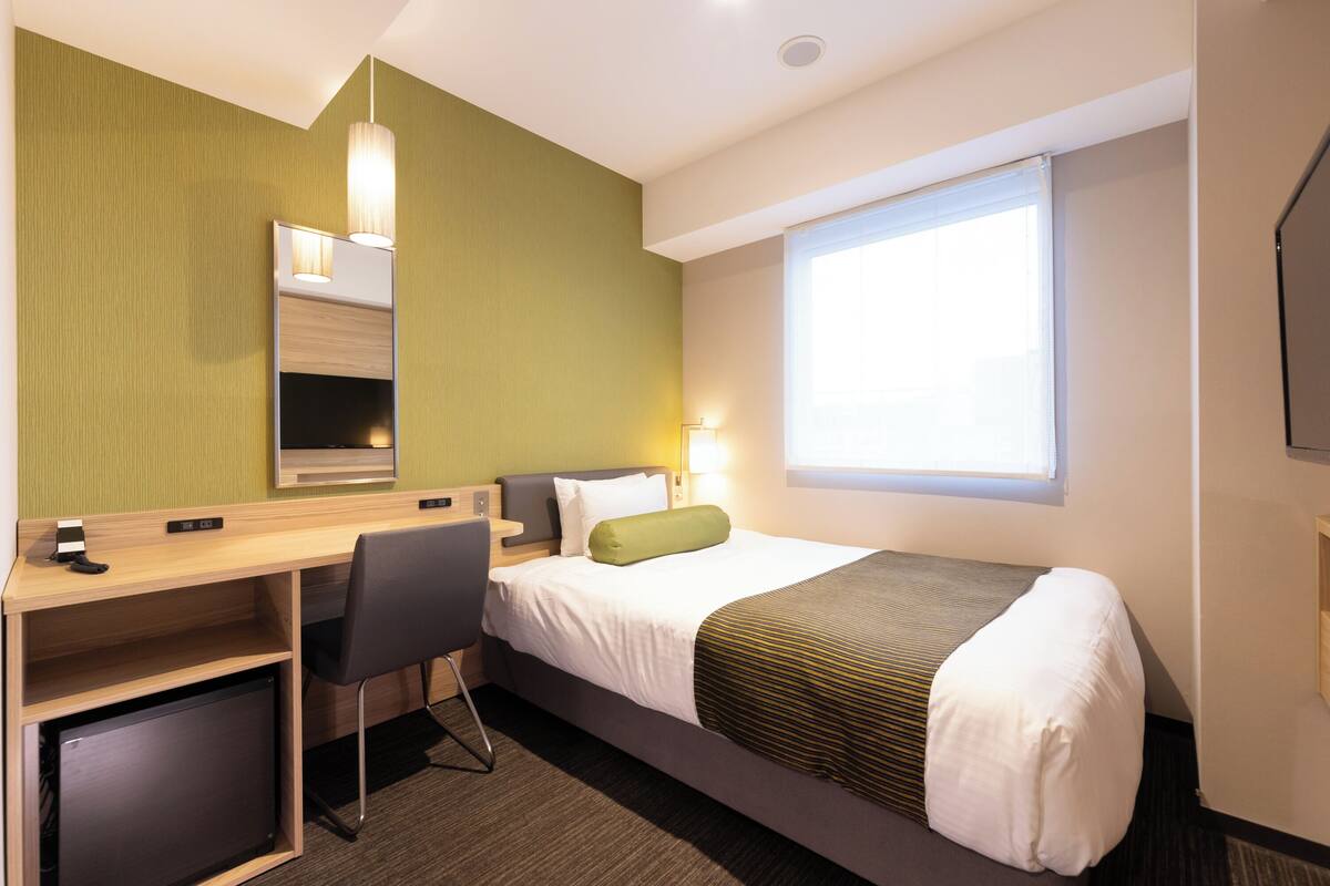 A hotel room with a bed, desk, chair, and a window.