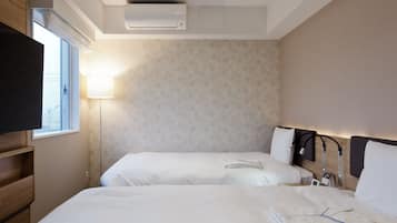Hotellihuone, jossa on kaksi sänkyä, televisio, yöpöytälamppu ja seinälle asennettu ilmastointilaite.