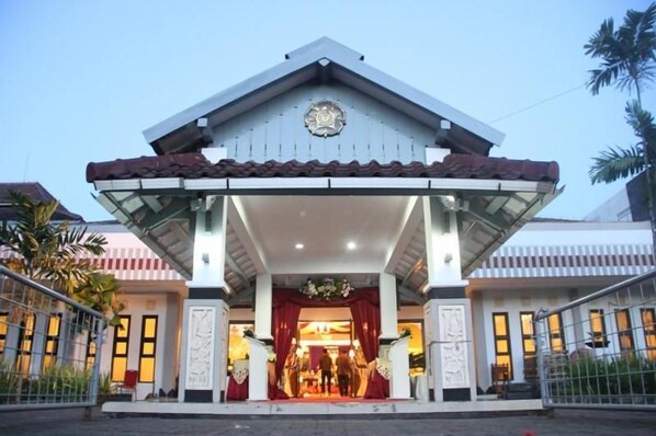 A hotel entrance with a covered entrance, a clock, and a red awning. - University Club Hotel UGM (Yogyakarta)
