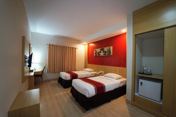 A hotel room with two beds, a desk, a chair, a small refrigerator, and a mirror. - University Club Hotel UGM (Yogyakarta)