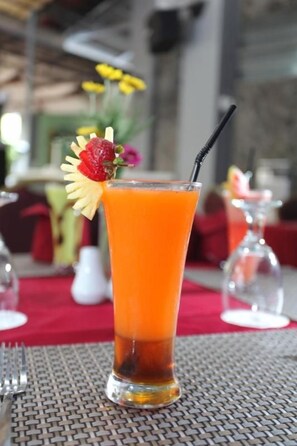 A tall glass of orange juice with a strawberry garnish and a black straw on a table with a woven placemat. - University Club Hotel UGM (Yogyakarta)