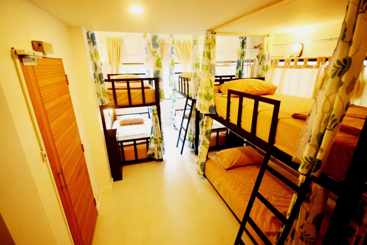 A dormitory room with bunk beds, a wooden wardrobe, and a small table.